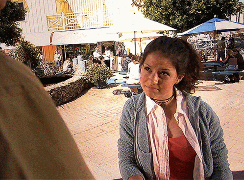 A Woman Wearing A Choker And A Blue Sweater Stands In Front Of A Restaurant GIF