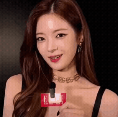 A Woman Wearing A Choker And Earrings Is Holding A Microphone And Smiling . GIF