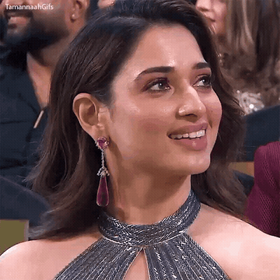 A Woman Wearing A Choker And Earrings Is Smiling And Looking At The Camera . GIF