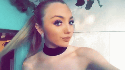 A Woman Wearing A Choker And Earrings Takes A Selfie GIF