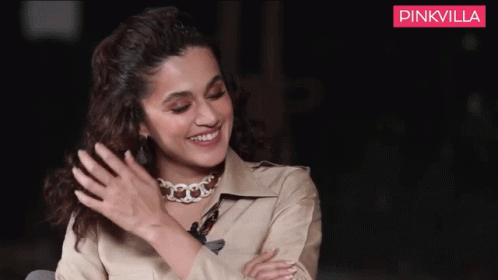 A Woman Wearing A Choker Is Smiling In Front Of A Pinkvilla Ad GIF