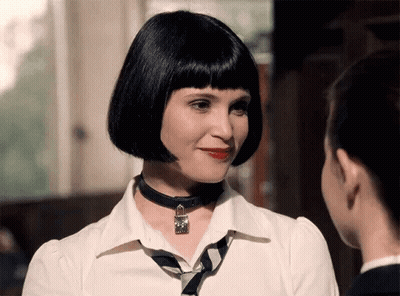 A Woman Wearing A Choker Necklace And A White Shirt Looks At Another Woman GIF