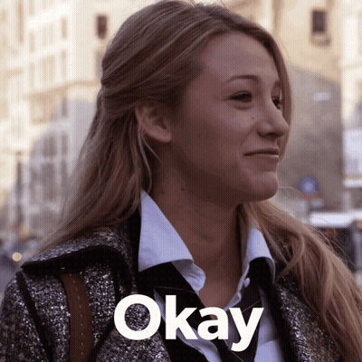 A Woman Wearing A Coat And Tie Is Smiling With The Word Okay Below Her GIF