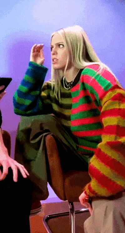 A Woman Wearing A Colorful Striped Sweater Is Sitting In A Chair GIF