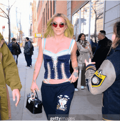 A Woman Wearing A Corset Top And Sweatpants Walking Down A Street GIF