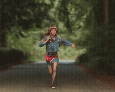 A Woman Wearing A Cowboy Hat And A Denim Jacket Runs Down A Road GIF