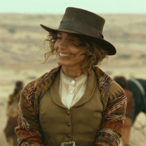 A Woman Wearing A Cowboy Hat And A Vest Is Smiling GIF