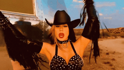 A Woman Wearing A Cowboy Hat And Fringe Gloves GIF