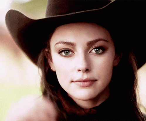 A Woman Wearing A Cowboy Hat Is Looking At The Camera . GIF