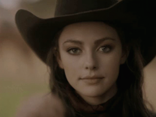 A Woman Wearing A Cowboy Hat Looks At The Camera . GIF
