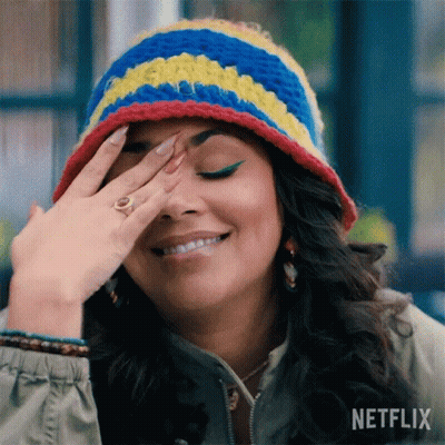 A Woman Wearing A Crocheted Hat And A Ring Is Smiling And Covering Her Face With Her Hand . GIF