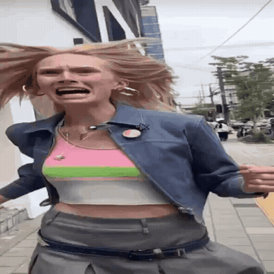 A Woman Wearing A Crop Top And A Denim Jacket Is Running Down A Street GIF