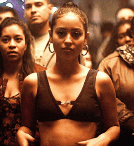 A Woman Wearing A Crop Top And Hoop Earrings Stands In A Crowd GIF