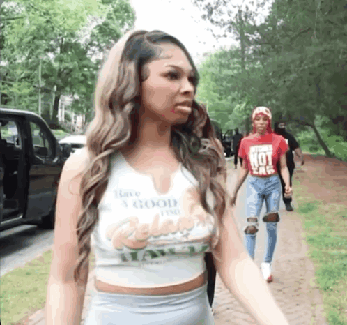 A Woman Wearing A Crop Top That Says Have A Good Time Is Walking Down A Sidewalk . GIF