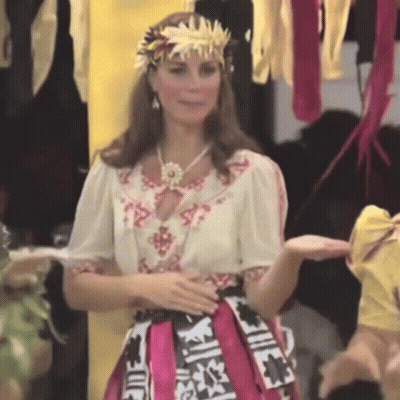 A Woman Wearing A Crown And A Pink Skirt Is Standing In Front Of A Group Of People . GIF