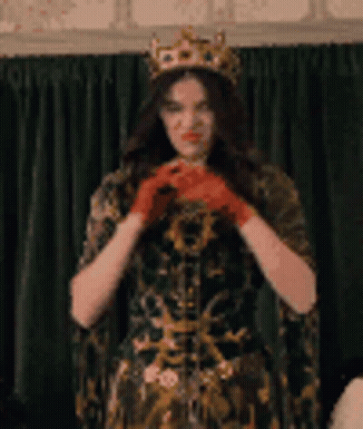 A Woman Wearing A Crown And Red Gloves Is Standing In Front Of A Curtain . GIF