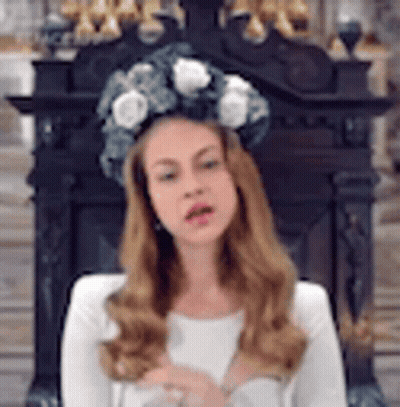 A Woman Wearing A Crown Of Flowers On Her Head Is Sitting In Front Of A Fireplace . GIF