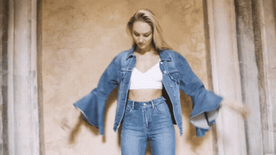 A Woman Wearing A Denim Jacket And Jeans Is Dancing GIF