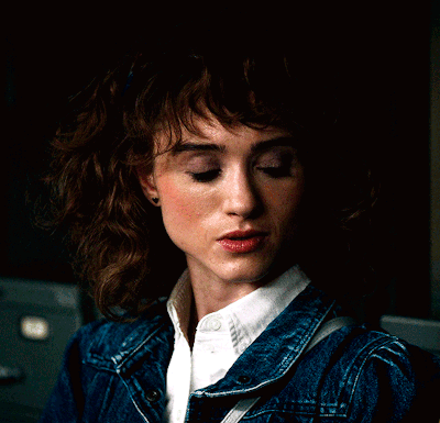 A Woman Wearing A Denim Jacket And White Shirt Looks Down GIF