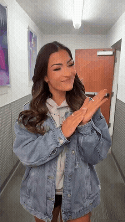 A Woman Wearing A Denim Jacket Is Standing In A Hallway . GIF