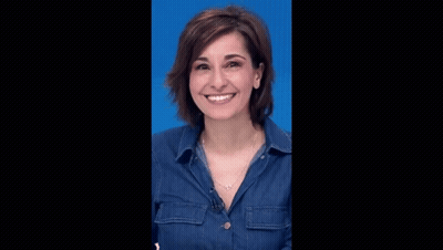 a woman wearing a denim shirt and a necklace is smiling against a blue background .