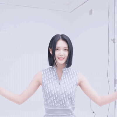 A Woman Wearing A Dior Sleeveless Top Smiles With Her Hands In The Air GIF