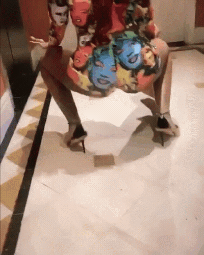 A Woman Wearing A Dress With Faces On It Is Dancing On The Floor GIF