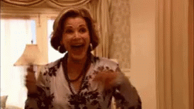 A Woman Wearing A Floral Shirt And A Necklace Is Standing In A Room . GIF