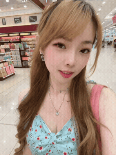 A Woman Wearing A Floral Top And A Butterfly Necklace Takes A Selfie GIF