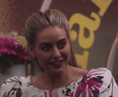 A Woman Wearing A Floral Top Smiles In Front Of A Sign That Says ' A ' GIF