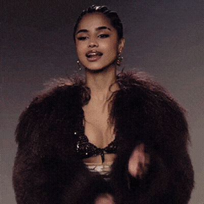 A Woman Wearing A Fur Coat And A Bra Is Singing GIF