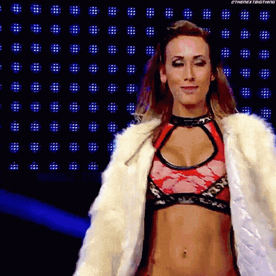 A Woman Wearing A Fur Coat And A Bra Is Walking On A Stage . GIF