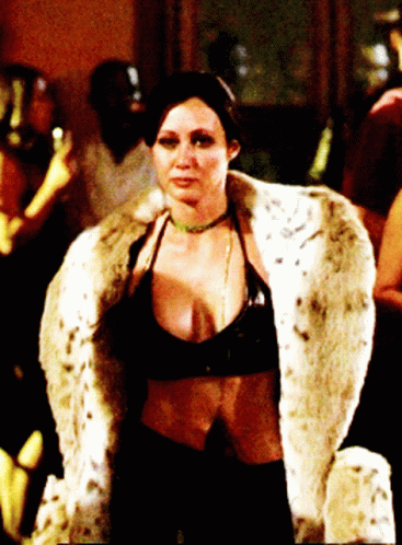 A Woman Wearing A Fur Coat And A Choker Stands In A Dark Room GIF
