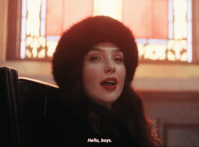 A Woman Wearing A Fur Hat Says Hello Boys In Front Of A Stained Glass Window GIF