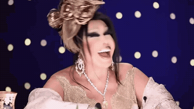 A Woman Wearing A Gold Dress And A Necklace Is Smiling And Laughing . GIF