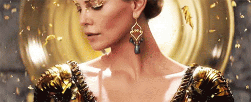 A Woman Wearing A Gold Dress And Earrings Is Standing In Front Of A Mirror . GIF