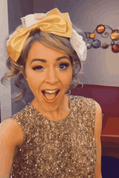 A Woman Wearing A Gold Sequined Dress And A Yellow Bow In Her Hair GIF