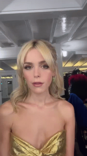 A Woman Wearing A Gold Strapless Dress Is Looking At The Camera GIF
