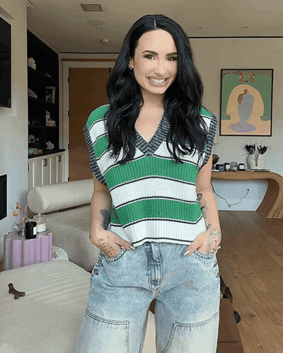 A Woman Wearing A Green And White Striped Vest And Jeans Smiles For The Camera GIF