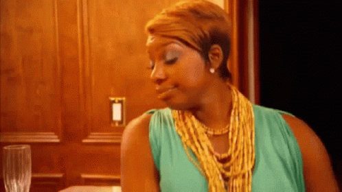A Woman Wearing A Green Dress And A Gold Necklace Is Sitting At A Table GIF