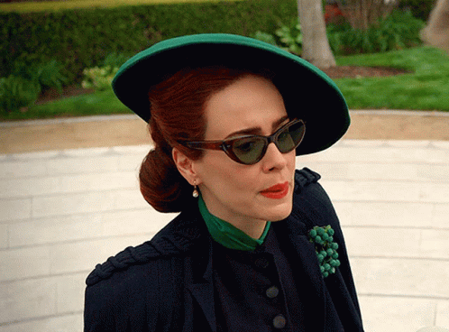 A Woman Wearing A Green Hat And Sunglasses Looks To Her Left GIF