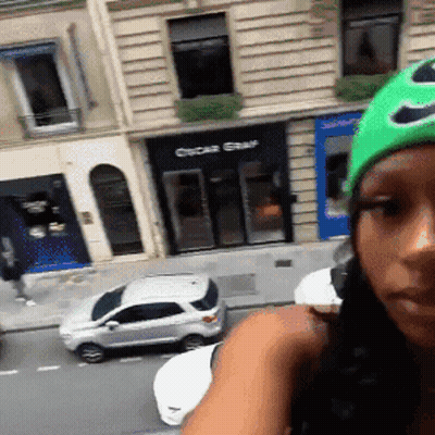 A Woman Wearing A Green Hat Is Standing In Front Of A Store That Says Oscar Star GIF
