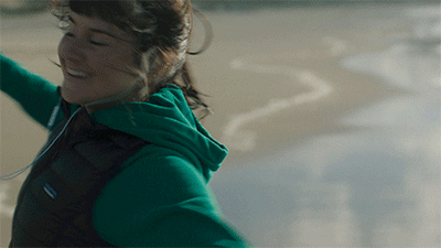 A Woman Wearing A Green Patagonia Vest Is Smiling On The Beach GIF