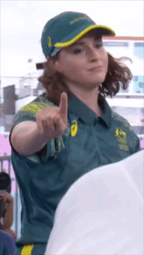 A Woman Wearing A Green Shirt And A Hat Is Pointing At The Camera GIF
