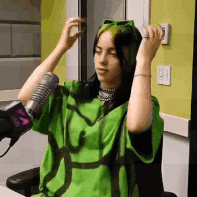 A Woman Wearing A Green Shirt Is Sitting In Front Of A Microphone GIF