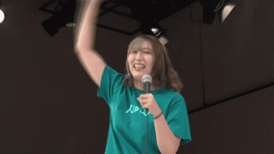 A Woman Wearing A Green Shirt That Says Zip On It Is Holding A Microphone GIF