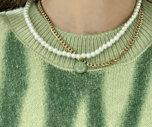 A Woman Wearing A Green Sweater And A Necklace With A Smiley Face On It . GIF