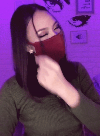A Woman Wearing A Green Sweater And A Red Mask With A Purple Background GIF