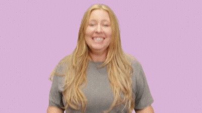 A Woman Wearing A Grey T-Shirt Is Smiling With Her Hands Outstretched GIF