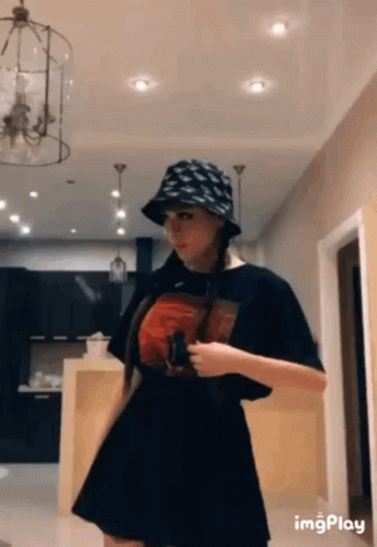 A Woman Wearing A Hat And A Black Skirt Is Standing In A Room . GIF